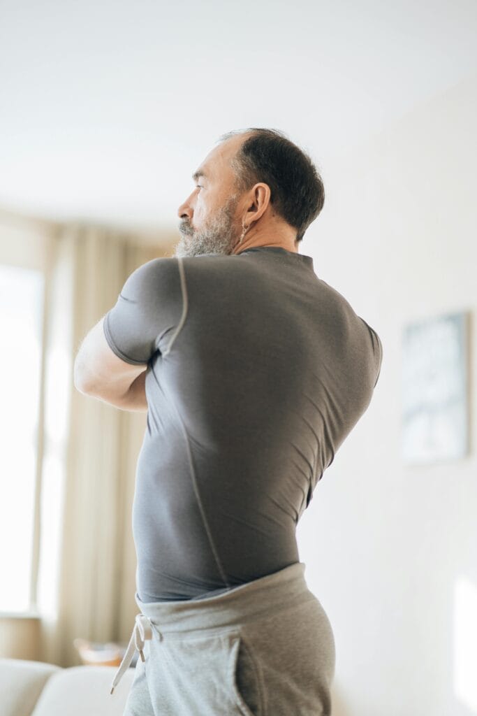 Elderly man in activewear stretching indoors for healthy living and fitness.