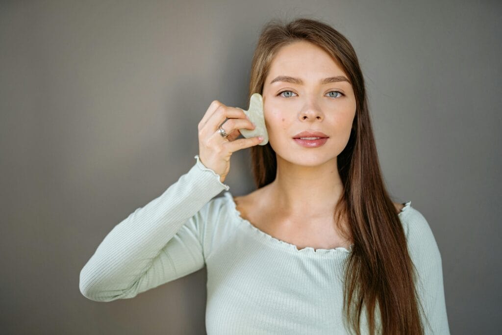 A woman uses a jade gua sha tool for facial massage, promoting self-care and beauty routines. | Want Firmer Skin After 30? This Collagen Trick Works Better Than Creams