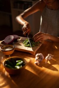A person chopping cilantro with fresh ingredients on a wooden board in warm kitchen lighting. | Want Glowing Skin and Stronger Immunity? These 10 Foods Supercharge Your Glutathione Naturally