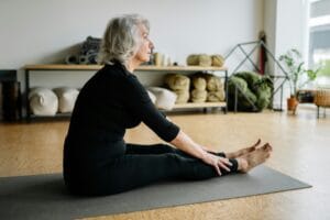 Senior woman in black clothing doing yoga stretching on a yoga mat indoors. | Doctor Shocked: The Simple Routine That Helped This 65-Year-Old Throw Away Her Cane