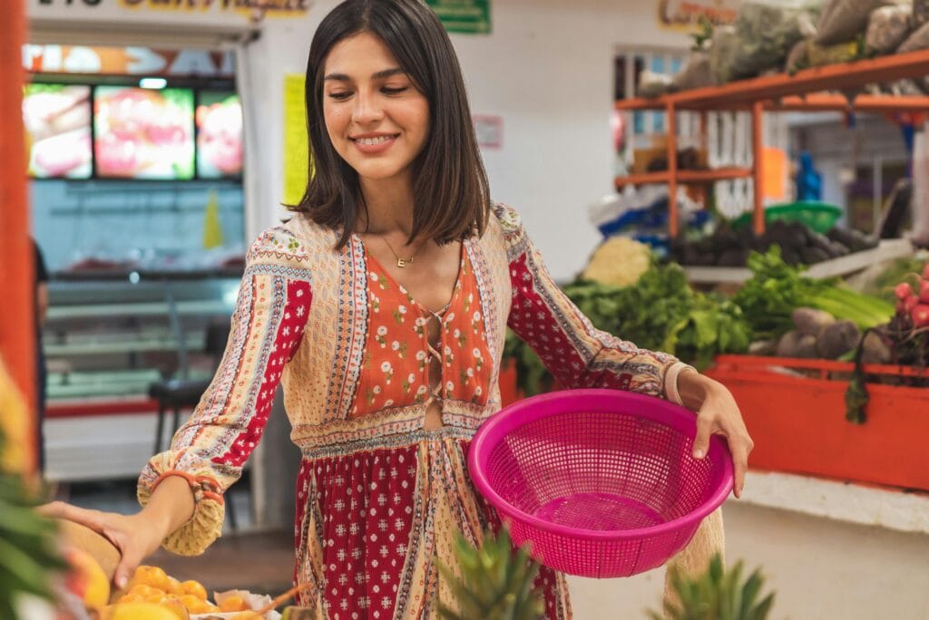 Smiling woman with a pink basket selecting fresh produce at a local market.