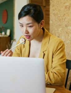 An adult woman enjoying sushi with chopsticks while engaging with a laptop indoors. | Want a Sharper Mind? These 10 Superfoods Are Dietitian-Approved for Brainpower