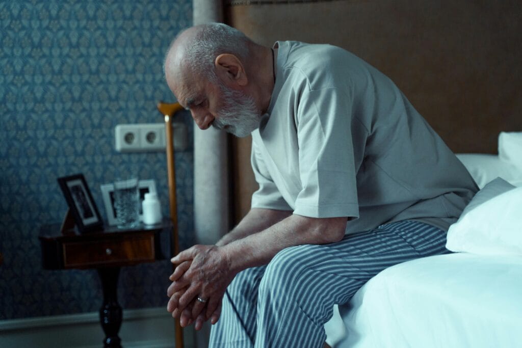An elderly man sits thoughtfully on a bed, conveying solitude and reflection.