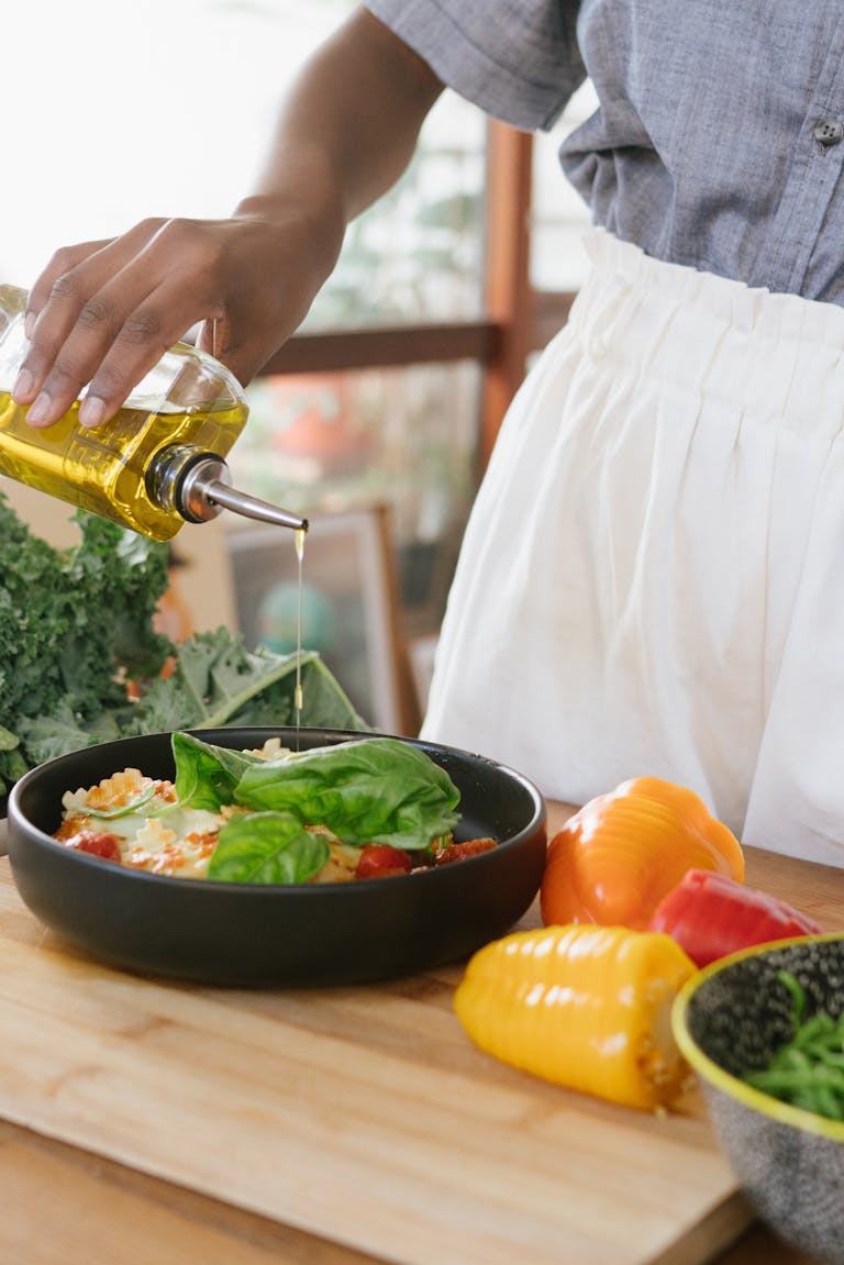 Person drizzles olive oil over fresh vegetable salad on a wooden cutting board. | The Heart-Healthy Oil That Could Lower Your Cholesterol—Backed by New Research