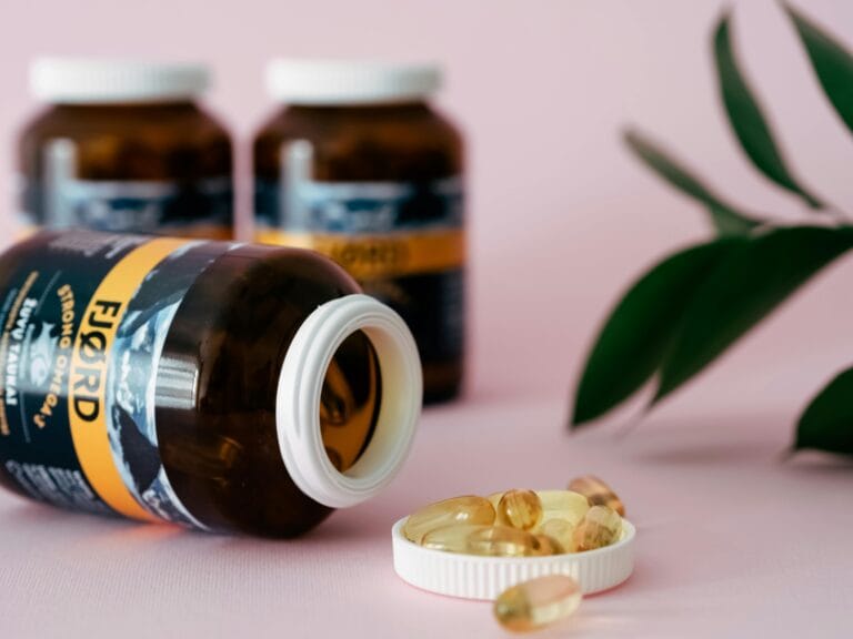 Close-up of omega-3 or fish oil capsules and bottles on a pink background, ideal for health and wellness themes.