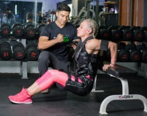 Woman doing tricep dips with personal trainer support in a gym setting.