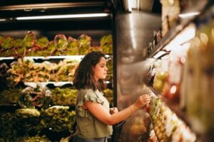 A woman selecting fresh vegetables from a supermarket aisle.
