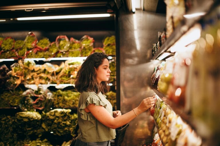 A woman selecting fresh vegetables from a supermarket aisle.