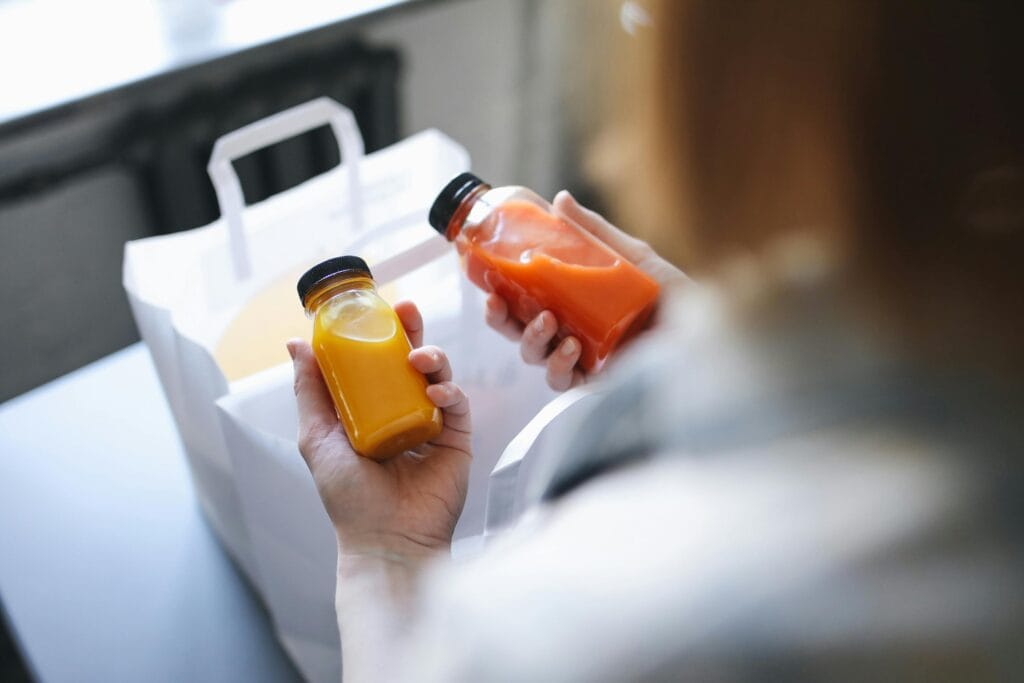 Hands holding bottled fruit juices indoors, perfect for food delivery concept.
