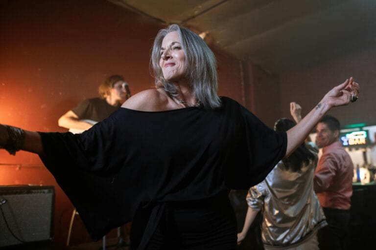 A joyful woman dancing in a lively nightclub scene filled with people and energy.