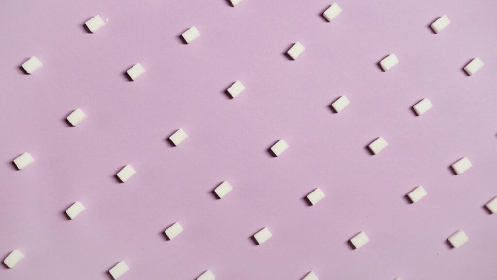 Geometric arrangement of white sugar cubes on a pastel pink surface.
