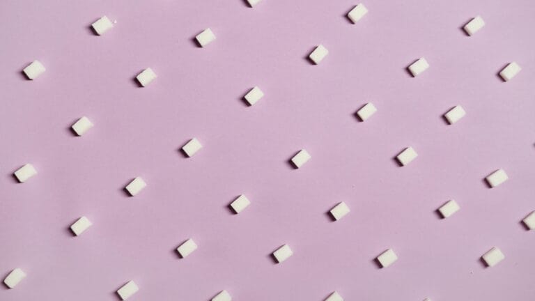 Geometric arrangement of white sugar cubes on a pastel pink surface.