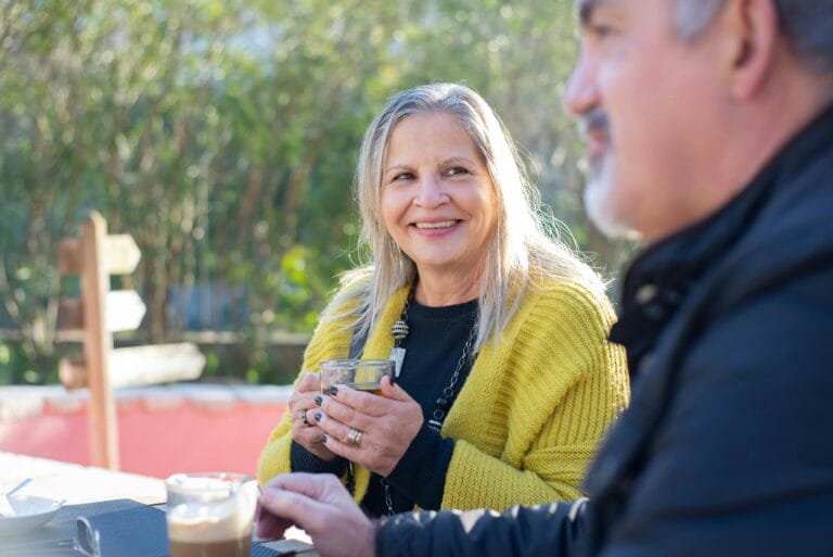 Senior couple smiling and chatting over coffee in a sunny park setting. | Scientists Are Buzzing About This Tea + Vitamin Duo That Rejuvenates Aging Brain Cells
