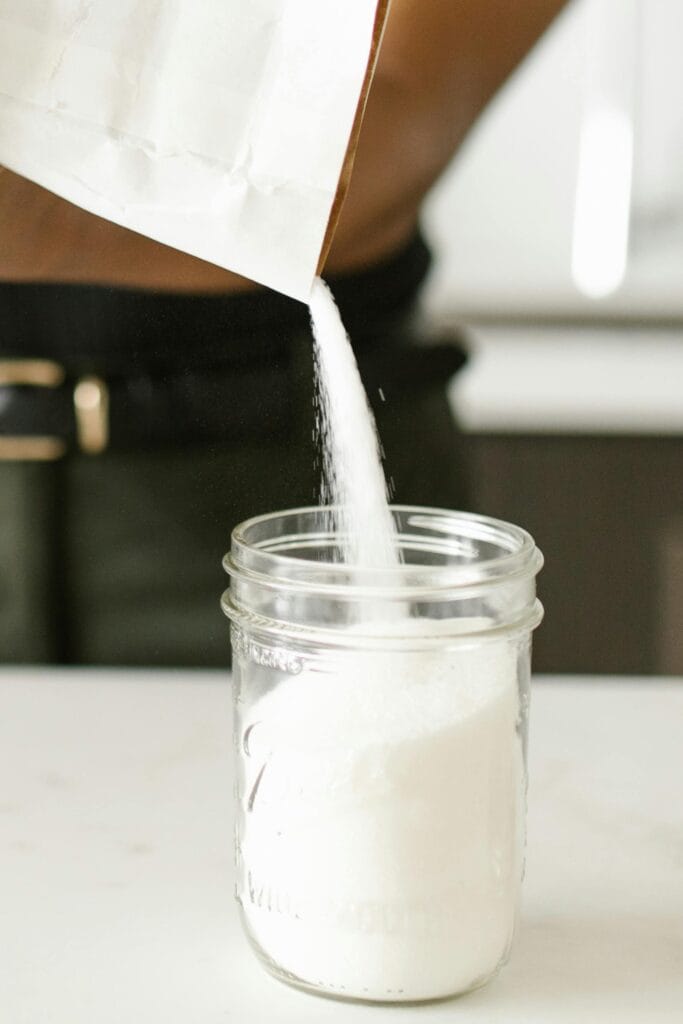 Close-up of person pouring sugar into a glass jar on a kitchen counter, showing organization.