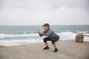 A senior woman performs squats outdoors by the ocean, embodying a healthy and active lifestyle.