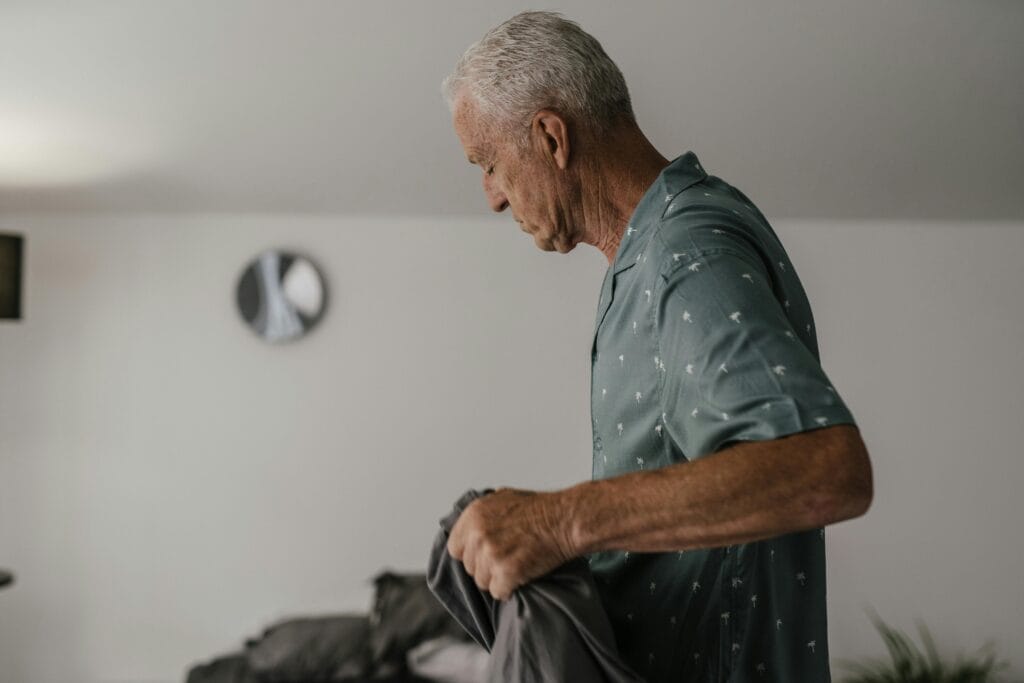 Senior man with gray hair holding a blanket indoors, side view.