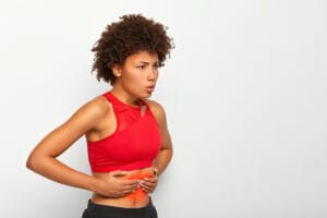 woman holding gut in pain | New Study Links These 5 Gut Issues to Alzheimer’s—What You Eat Could Be Hurting Your Brain