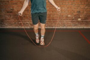 Man exercising with jump rope indoors against brick wall background.