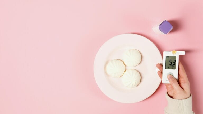 Flat lay of glucose meter and white sweets on a pink background, symbolizing diabetes awareness.