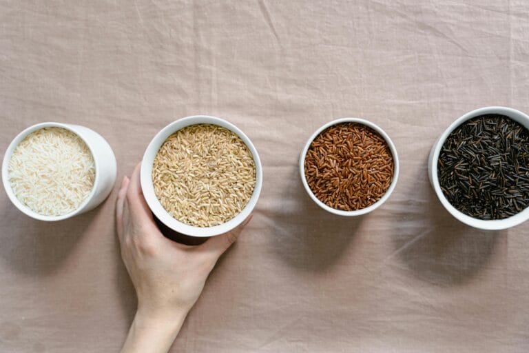 Flat lay showcasing four types of rice in cups on a neutral surface.