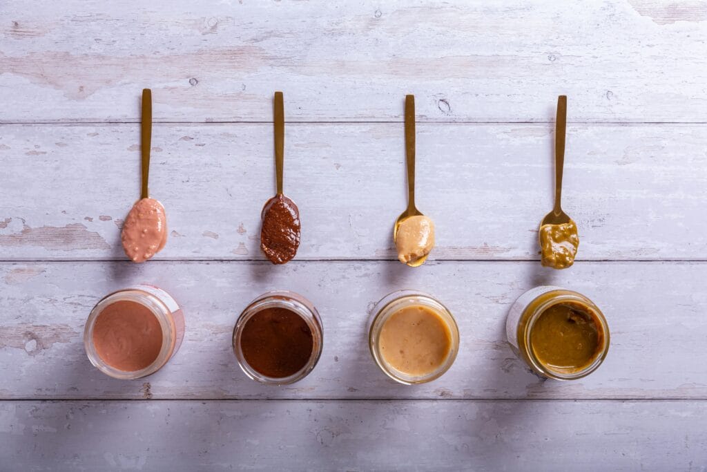 Top view of various nut butters in jars and spoons on a wooden surface.