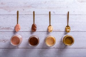 Top view of various nut butters in jars and spoons on a wooden surface.