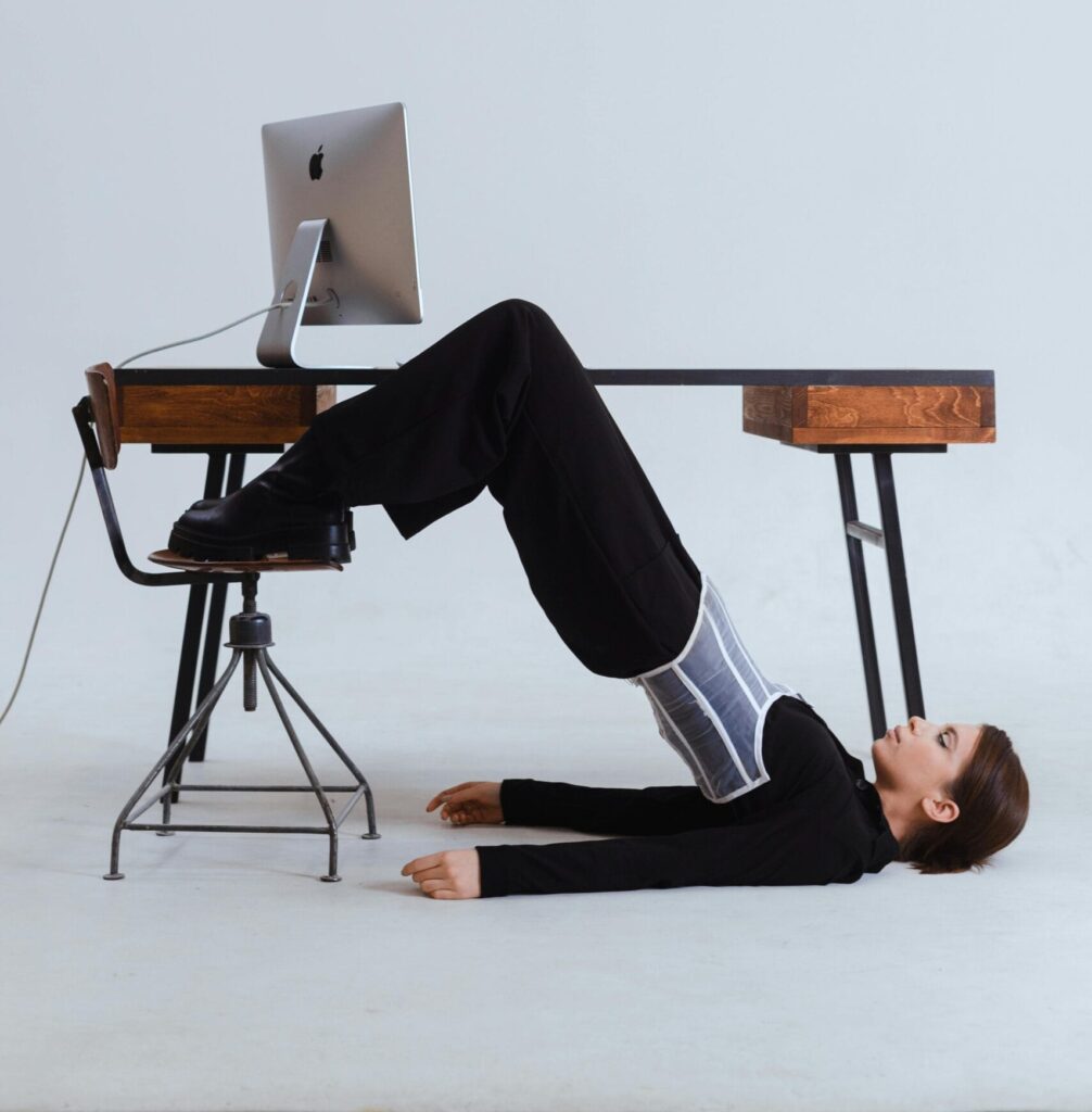 Woman in an innovative stretch position under an office desk, blending flexibility with workplace setting.