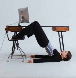 Woman in an innovative stretch position under an office desk, blending flexibility with workplace setting.