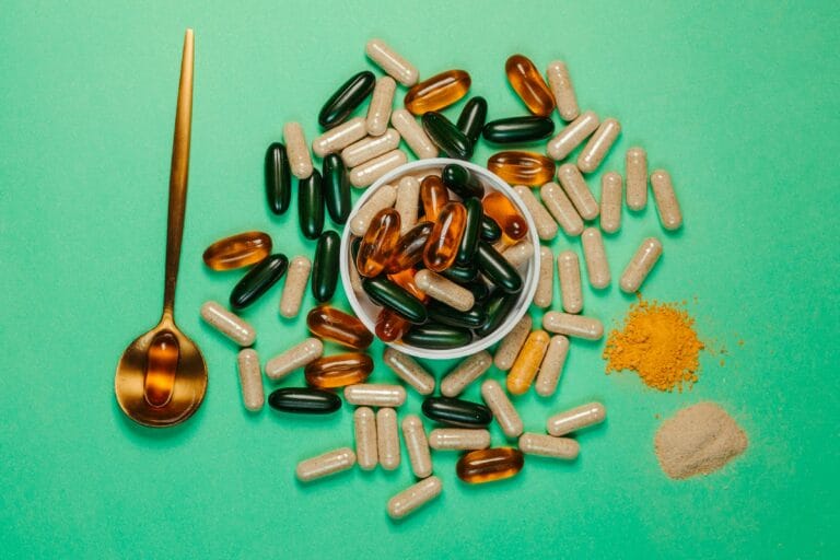 A vibrant assortment of capsules and powders on a green background with a golden spoon.
