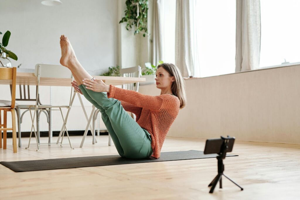 Woman doing a yoga pose indoors, using a smartphone to record or follow along.