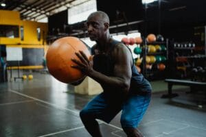 Focused mature man in gym squatting with a medicine ball during a workout.