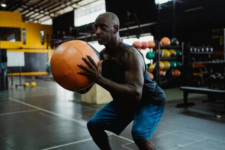 Focused mature man in gym squatting with a medicine ball during a workout.