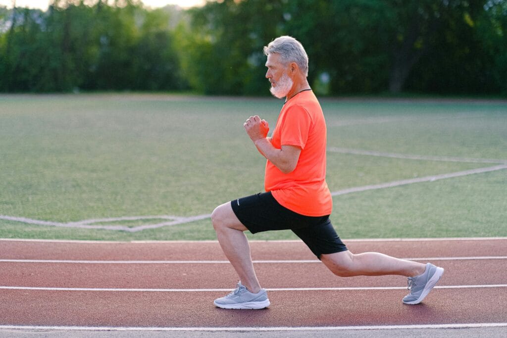Side view of bearded male training and doing lunges on track on blurred background of greenery