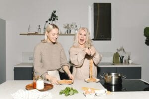 A joyful mother and daughter duo preparing spaghetti in a modern kitchen.