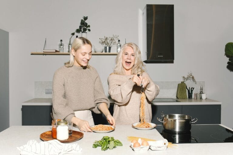 A joyful mother and daughter duo preparing spaghetti in a modern kitchen.