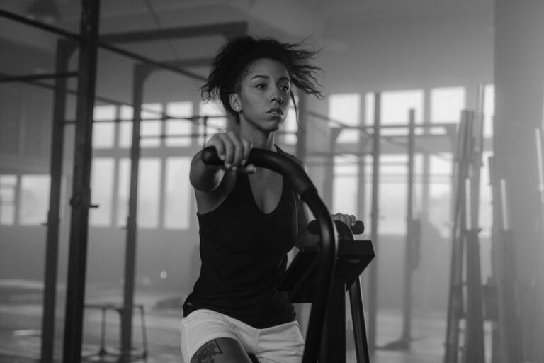 A determined woman working out on an air bike in a monochrome gym setting.
