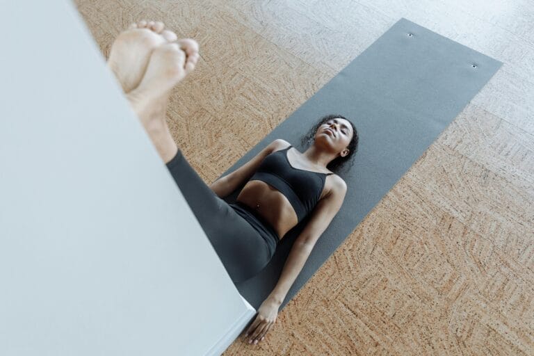 Woman lying on a yoga mat indoors, focusing on relaxation and flexibility.