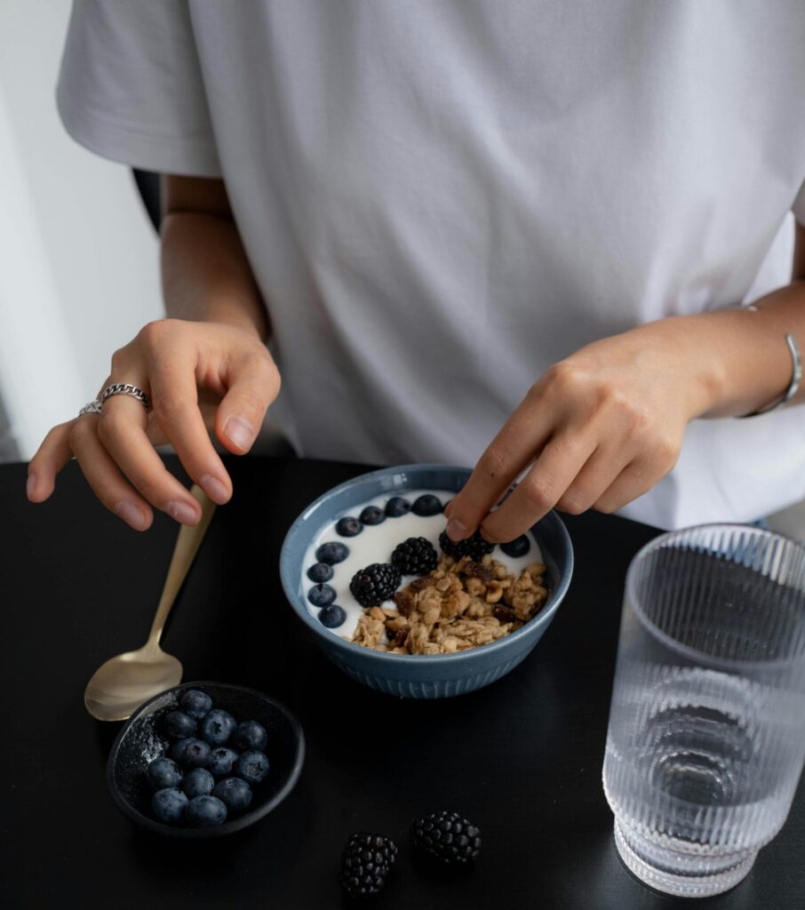 High-angle shot of a person preparing a berry and granola breakfast, emphasizing healthy eating.
