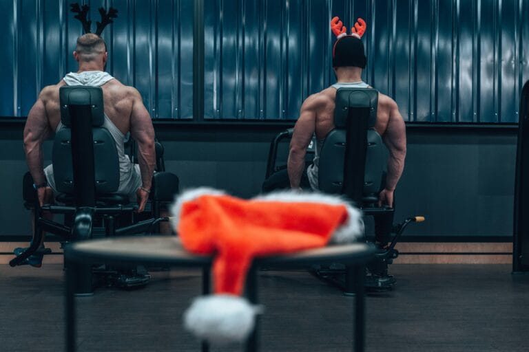 Two muscular men workout in the gym wearing festive reindeer antlers, adding a holiday touch.