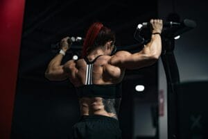 Back view of a muscular woman lifting weights in a gym, showcasing strength and determination.