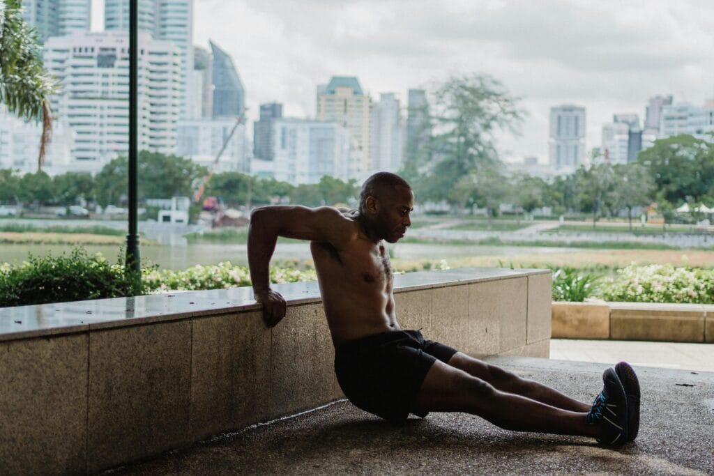 A fit man performs tricep dips in an urban park with a city skyline backdrop, embracing strength and wellness.