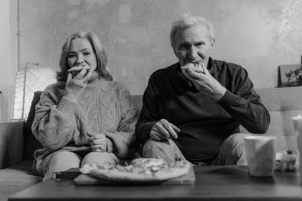 Black and white photo of senior couple enjoying pizza together on a cozy couch.