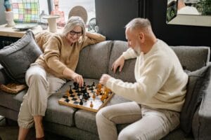 Senior couple playing chess on a cozy couch, embracing leisure time together indoors.