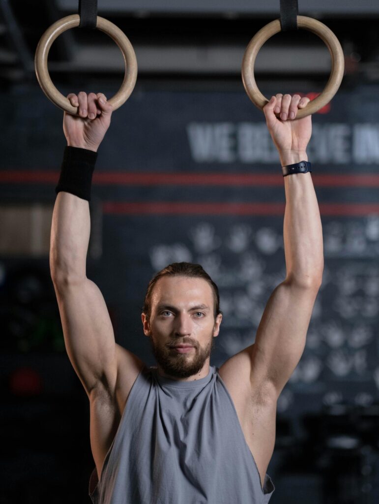 A male athlete performing strength training exercises on gymnastic rings in a gym setting. dead hang, pull up