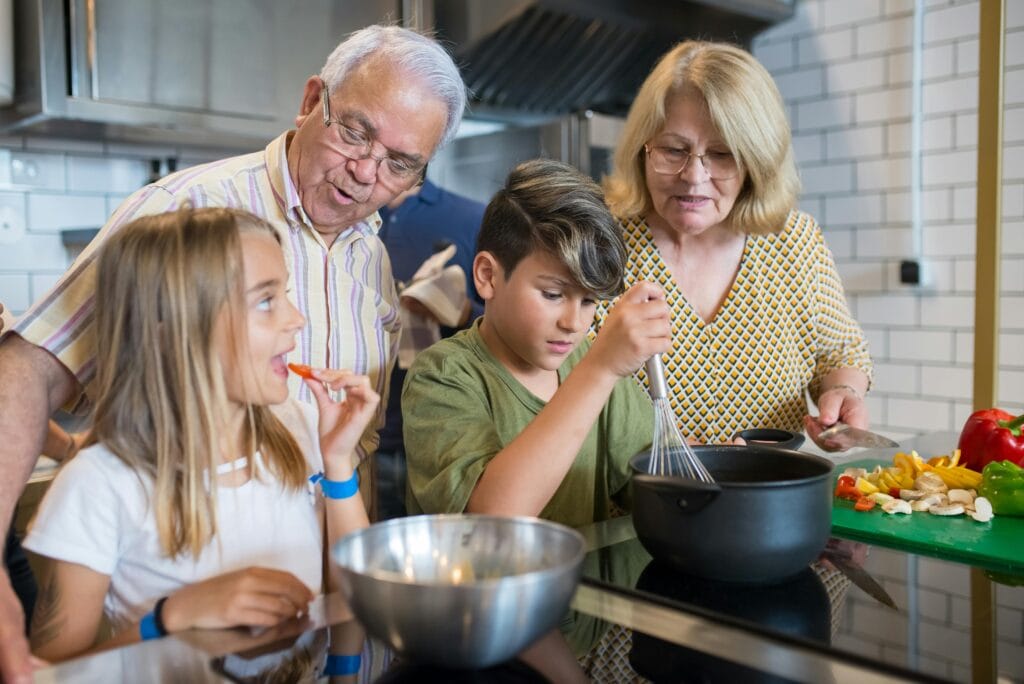 Grandparents teaching grandchildren to cook in a modern kitchen, sharing family time and culinary skills.