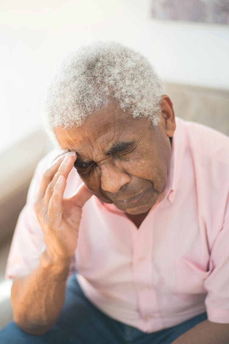 An elderly man with white hair showing sadness and grief with hand on face.