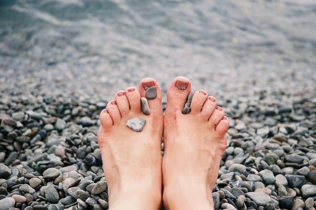 Close-up of female feet with stones on pebbled beach by the water, evoking relaxation and tranquility.