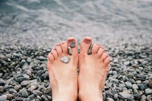 Close-up of female feet with stones on pebbled beach by the water, evoking relaxation and tranquility.