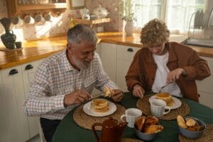 Elderly man and teenager sharing pancakes in a cozy kitchen setting, enjoying quality time together.