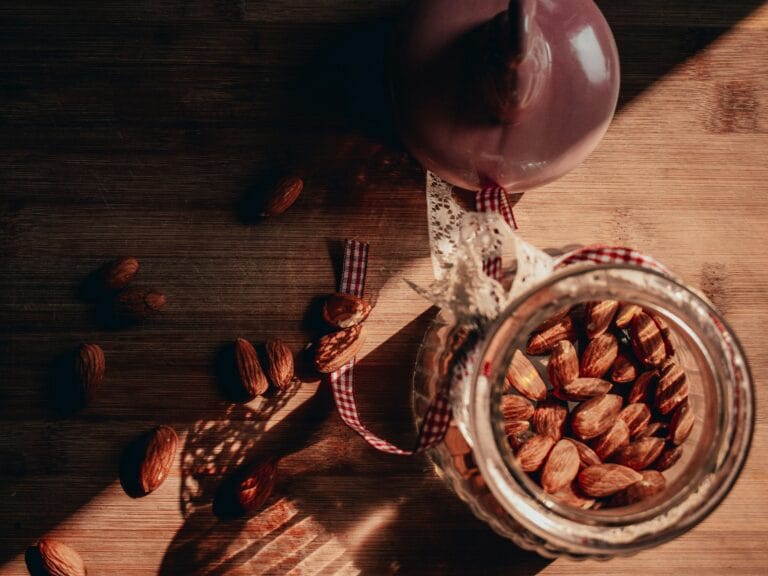 Rustic photo of almonds in a jar with warm lighting and shadows on a wooden table.